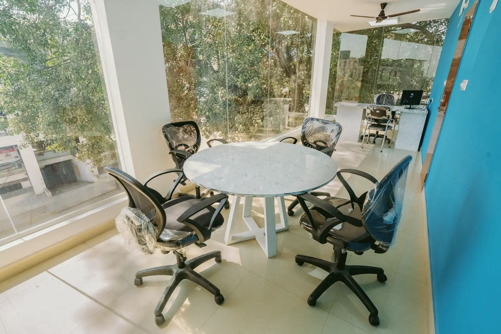 Round meeting table with mesh office chairs beside a full-height glass wall at Jakkur Workspaces, Bangalore, by Candidscape