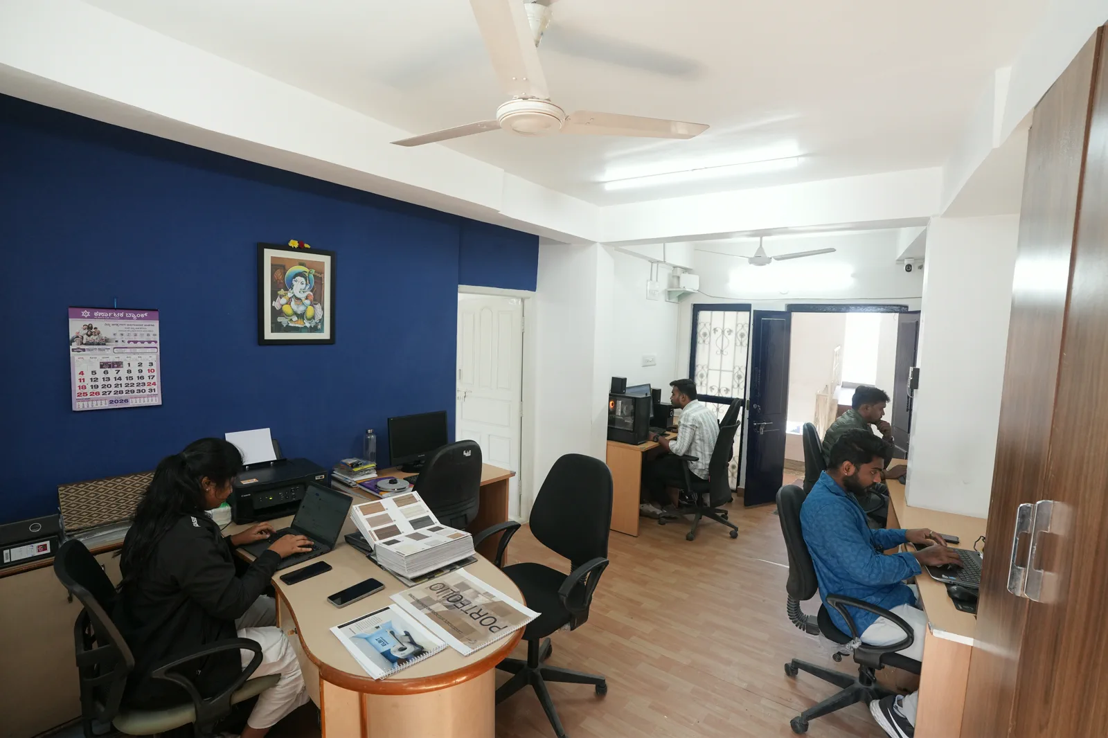 Working office at the Candidscape studio on New BEL Road, Bangalore, with staff at timber-finish desks in front of a navy feature wall